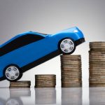 Close-up Of A Blue Car Over Rising Golden Stacked Coins